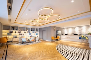 A hotel lobby with a checkered floor, a reception desk, and a seating area with chairs and tables. - Magnotel (Harbin)