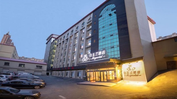 A multi-story hotel with a prominent glass facade and signage for a hotel and a restaurant. - Magnotel (Harbin)