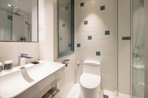 Un baño moderno con cabina de ducha de vidrio, un lavabo blanco con espejo y un inodoro.