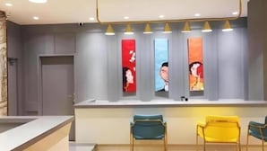 A reception area with a counter, three chairs, and a row of vertical artwork on the wall. - Magnotel (Harbin)