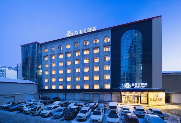 A hotel with a large parking lot and multiple floors with numerous windows. - Magnotel (Harbin)