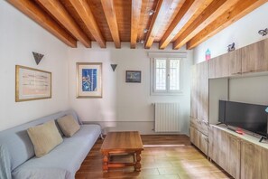 Una habitación con techo de madera, un sofá, una mesa, un televisor y una ventana.