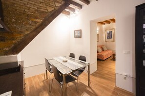 Un coin repas avec une table en verre, des chaises et une vue sur une chambre à coucher, où l’on aperçoit un lit et un tableau.
