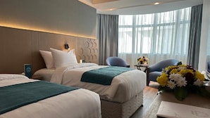 Habitación de hotel con dos camas, una mesita con un florero y un área de descanso con sillas.