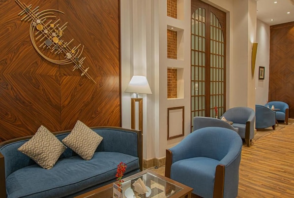 A hotel lobby with a blue sofa, armchairs, a lamp, and a decorative wall piece. - Grand Al Massa Hotel (Makkah)