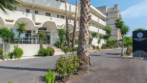 A multi-story hotel with a modern architectural design, featuring a prominent entrance with a sign, palm trees, and a well-maintained outdoor area. - Ixia Dream - Adults Only (Rhodes)