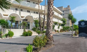 Um hotel de vários andares com design arquitetônico moderno, destacando uma entrada imponente com placa, palmeiras e área externa bem cuidada.