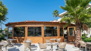 An outdoor dining area with tables and chairs, large windows, and a palm tree. - Ixia Dream - Adults Only (Rhodes)