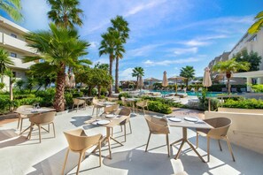 An outdoor dining area with tables and chairs, a pool, and palm trees. - Ixia Dream - Adults Only (Rhodes)