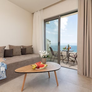 A modern living room with a sofa, a coffee table with fruit, and a view of the sea through a glass door. - Ixia Dream - Adults Only (Rhodes)