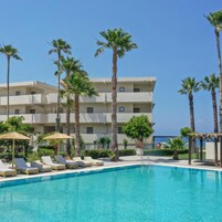 Un hotel con piscina, palmeras y sillas de descanso.