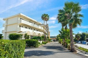 A multi-story hotel with a central courtyard, surrounded by palm trees and a clear sky. - Ixia Dream - Adults Only (Rhodes)
