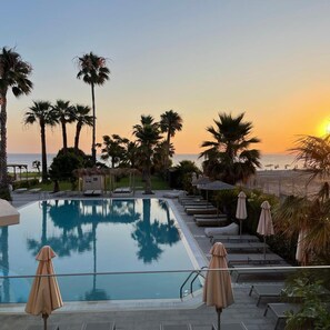 A poolside area with lounge chairs and umbrellas, palm trees, and a view of the ocean at sunset. - Ixia Dream - Adults Only (Rhodes)