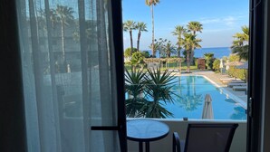 Un balcón con vistas a una piscina, palmeras y el océano.