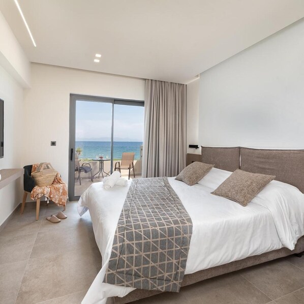 A hotel room with a large bed, a seating area with a table and chairs, and a view of the sea through a sliding door. - Ixia Dream - Adults Only (Rhodes)