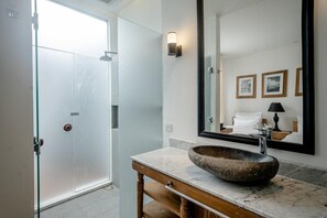 A bathroom with a large mirror, a wooden vanity, and a stone sink. - Gioheven Villa (Nusa Dua)