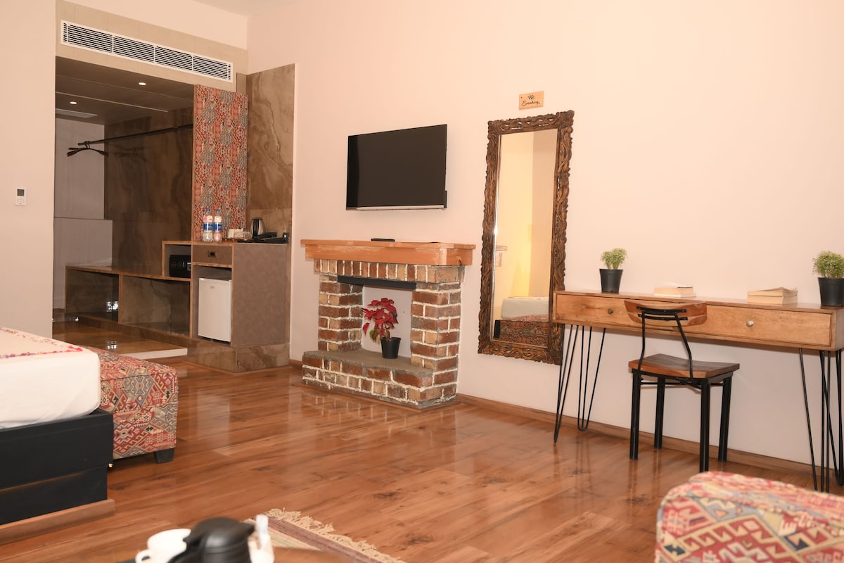 A modern room with a fireplace, a TV mounted on the wall, a desk with a chair, and a bed with patterned bedding.