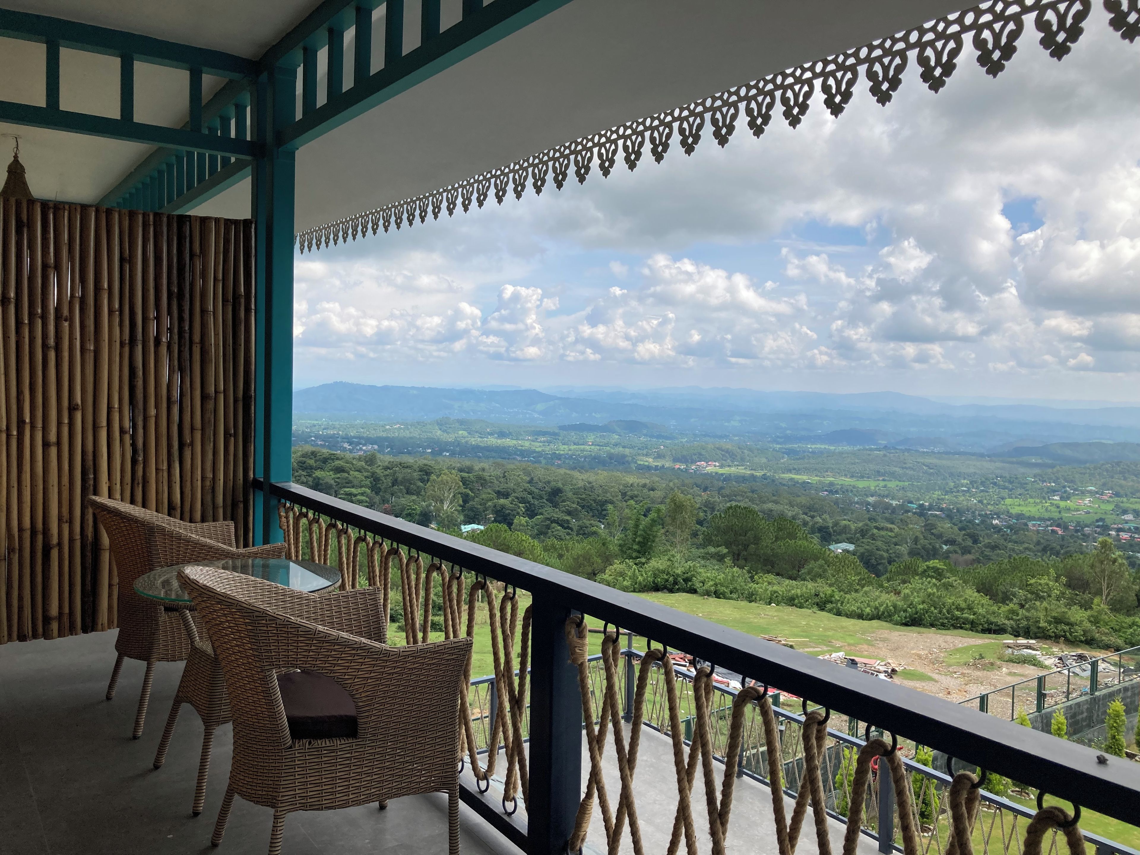 Un balcón con mobiliario de mimbre y vistas a un paisaje verde.