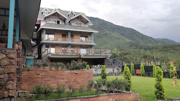 Um edifício com várias andares e varandas, rodeado por um jardim bem cuidado e uma paisagem montanhosa.