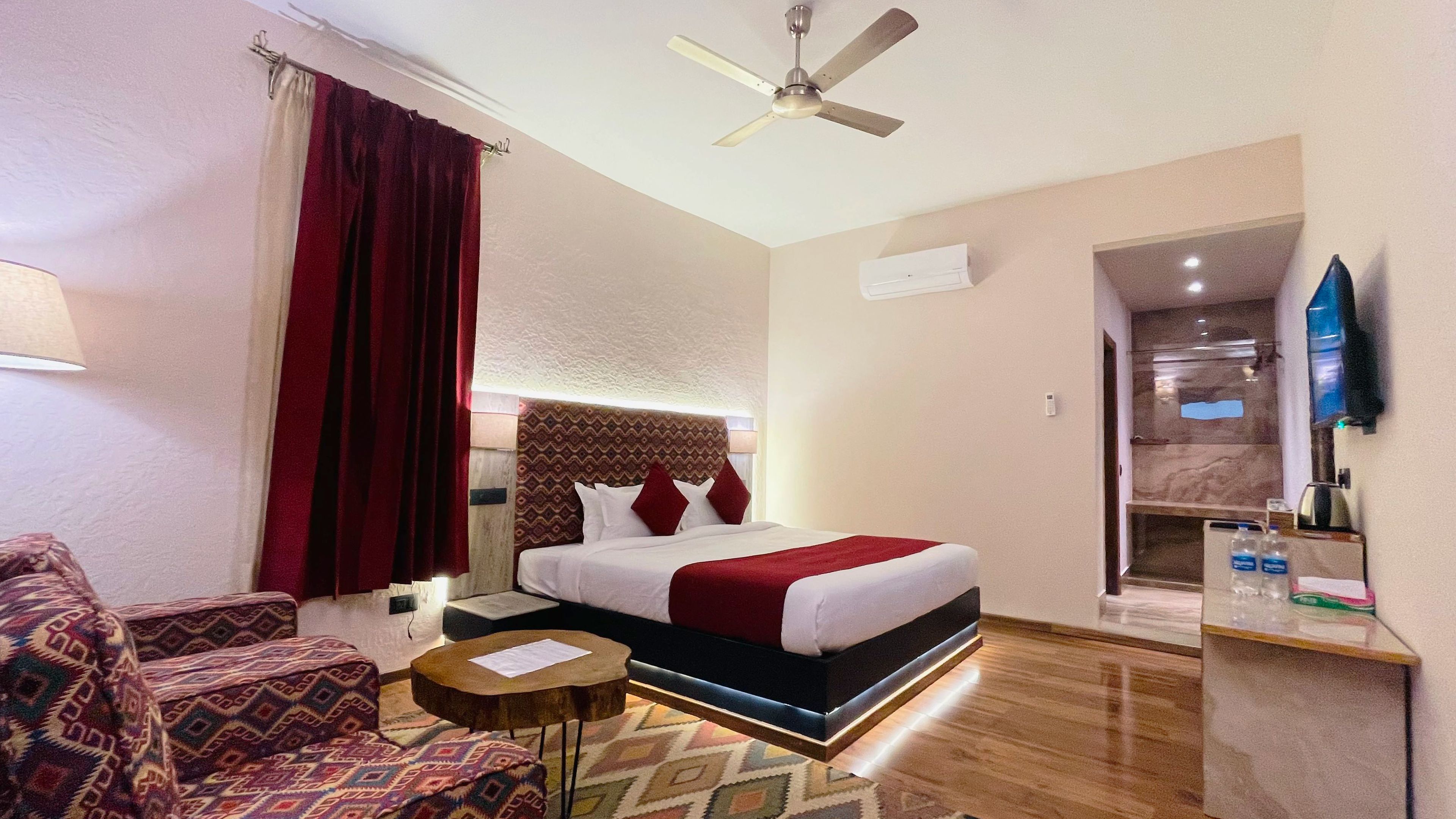 Habitación de hotel con cama, sofá, una mesita, ventilador de techo y televisor.