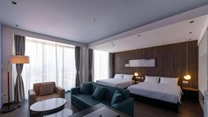 Una habitación de hotel moderna con una cama, dos sofás, una mesa de centro y un escritorio con una computadora portátil.