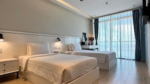 A hotel room with two beds, a bedside table, a lamp, and a window with curtains. - Grace Samudera Hotel Semporna (Semporna)