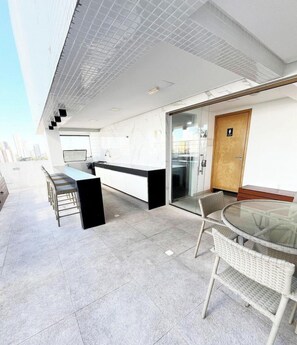 A modern kitchen with a bar area, a glass dining table, and a seating arrangement. - Manaira Apart Hotel por Carpediem (João Pessoa)