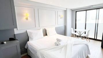 Quarto de hotel moderno com cama grande, mesas de cabeceira, escrivaninha e janela com vista.