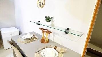 Uma área de refeições moderna com mesa de vidro, luminária pendente preta e dourada, e uma pequena planta em vaso sobre um prateleira de vidro.
