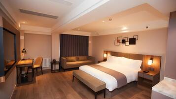 A modern hotel room with a large bed, a sofa, a desk, and a chair.