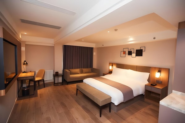 A modern hotel room with a large bed, a sofa, a desk, and a chair.