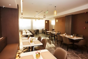 A hotel dining area with multiple tables and chairs, pendant lighting, and a view of the outdoors.