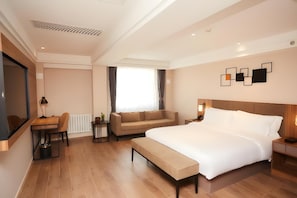 A modern hotel room with a large bed, a sofa, a desk, and a television.
