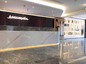 A hotel lobby with a marble reception desk, a wall-mounted sign, and a display of items.