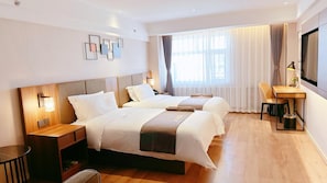 Quarto de hotel com duas camas, uma escrivaninha, uma cadeira, televisão e janela com cortinas.