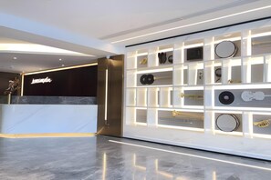 Um lobby de hotel moderno com uma mesa de recepção, uma parede com instrumentos musicais e piso lustroso.