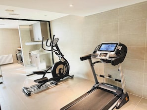 Un gimnasio en casa con una elíptica y una cinta de correr, una lavadora y un radiador.