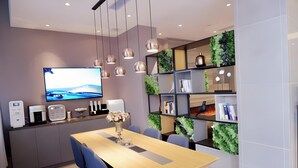 A modern dining area with a wooden table, blue chairs, a TV mounted on the wall, and green vertical gardens on the shelves. - Homeinn Selected (Guangzhou)