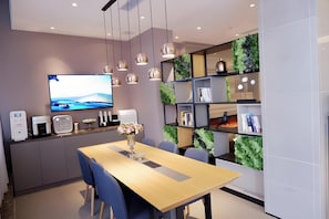 A modern dining area with a wooden table, blue chairs, a TV mounted on the wall, and green vertical gardens on the shelves. - Homeinn Selected (Guangzhou)