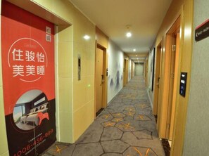 Un pasillo de hotel con alfombra estampada, puertas de madera y un anuncio rojo a la izquierda.