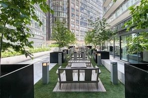 Un espacio al aire libre con mesas y sillas, rodeado de vegetación y edificios modernos.