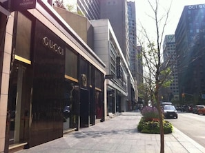 Vista de la calle con una tienda Gucci a la izquierda, acera y un árbol con flores.