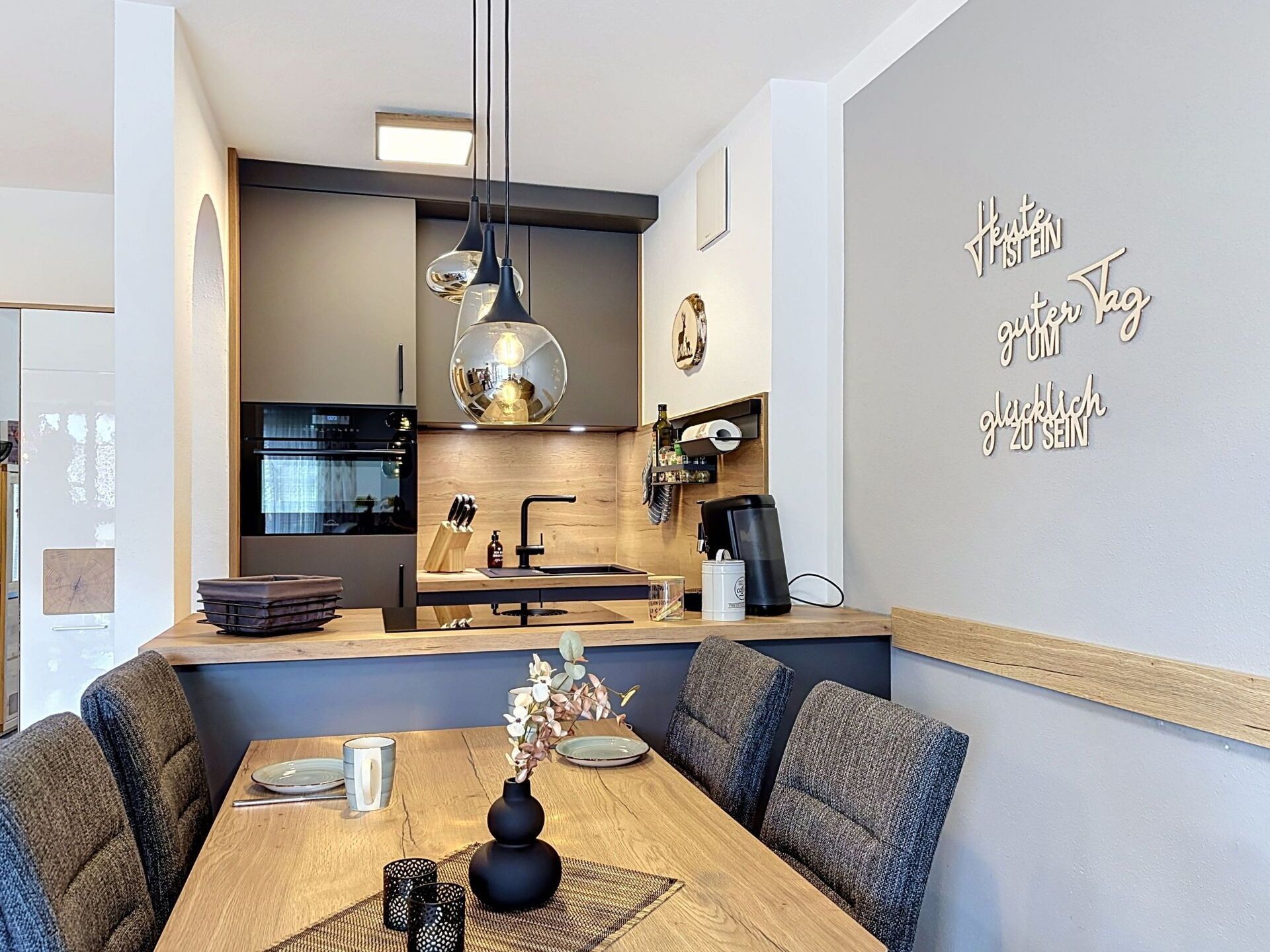 A modern kitchen with a dining area, featuring a wooden table, chairs, and a decorative wall with text.