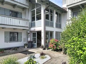 A two-story residential building with a balcony, a front door, and a small garden area with plants and a pathway. - Beautiful apartment for 4 guests with WIFI, pool, TV and terrace (Auerbach)