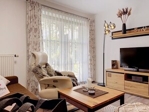 Un salon comprenant un canapé, un fauteuil, une table basse, un meuble pour la télévision et un lampadaire.