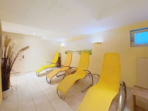 Ein Zimmer mit drei gelben Lounge-Sesseln, einem Heizkörper und einem an der Wand befestigten Fernseher.