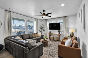 A modern living room with a leather sofa, a brown armchair, a round coffee table, and a ceiling fan. - Sleeps 16 | Hot Tub +Game Garage + Kids' Play Loft (Meridian)
