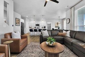 Ein modernes Wohnzimmer mit einer Ledersofa, einem Couchtisch mit einer Pflanze und einer Küche im Hintergrund.