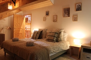 Quarto com teto de madeira, cama com roupa de cama estampada e mesa de cabeceira.