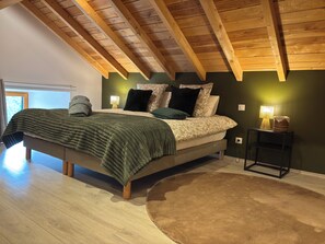 Ein Schlafzimmer mit Holzboden, einem Bett mit vielen Kissen, einem Nachttisch mit Lampe und einer grünen Wand.